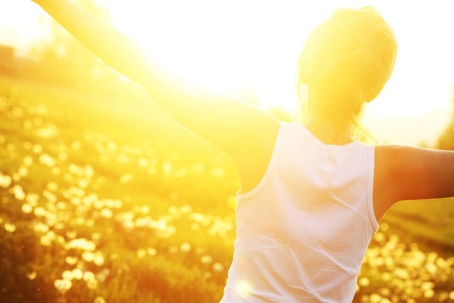 A person with arms outstretched stands in a sunny, golden field of flowers