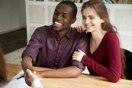 A smiling couple shakes hands with a person off-screen