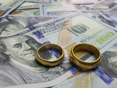 Two gold wedding rings sit on a pile of one-hundred dollar bills