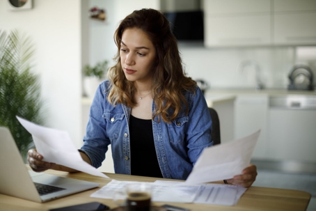 A young woman intently reviewing financial documents at a table with a laptop