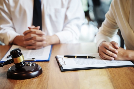 Two people sit at a table with legal documents, a gavel, and wedding rings.