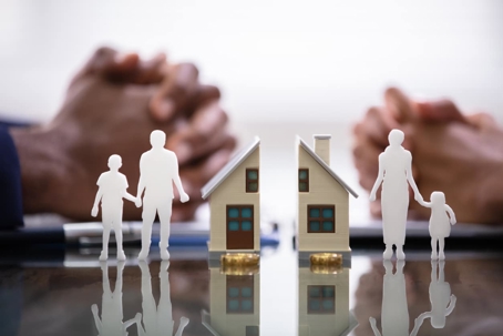 A model house is split in two, separating paper figures of a father and son from a mother and daughter