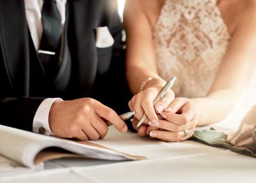 Couple signing wedding agreements. Visual concept for blog discussing prenuptial agreement vs postnuptial agreement.