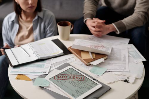Tablet with online financial document with past due stamp on screen lying on folder among other bills, receipts, notepad and young couple facing divorce and bankruptcy.