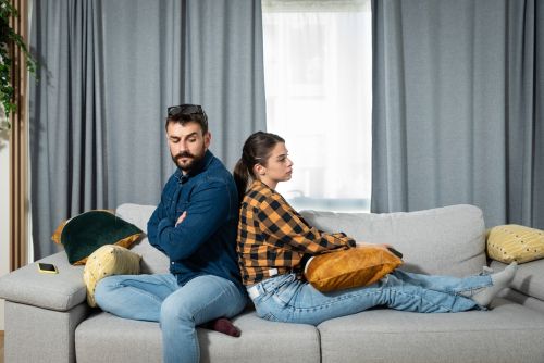 Young couple are arguing on the couch in their home and having difficulty and problems in a relationship and marriage sitting back to back and ignoring and not talking to each other