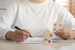 Woman holds back an inherited house while signing divorce papers. A visual concept for legal blog about protecting your inheritance during divorce.