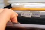 Close up of male hands searching through paperwork in a folder titled 