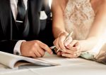 Couple signing wedding agreements. Visual concept for blog discussing prenuptial agreement vs postnuptial agreement.