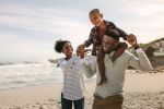 Parents carrying their son on shoulders on a beach vacation. - Law Office of Shelly Ingram